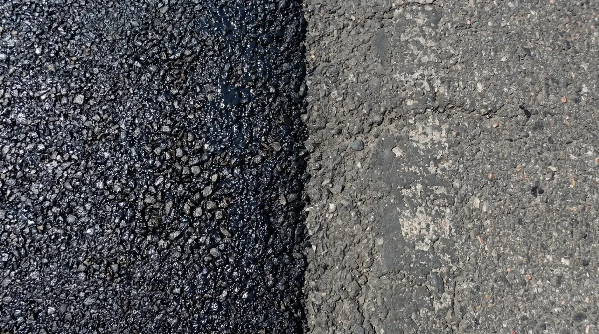 Close-up cross-section of fresh asphalt surface texture showing aggregate and bitumen binder in a newly paved driveway