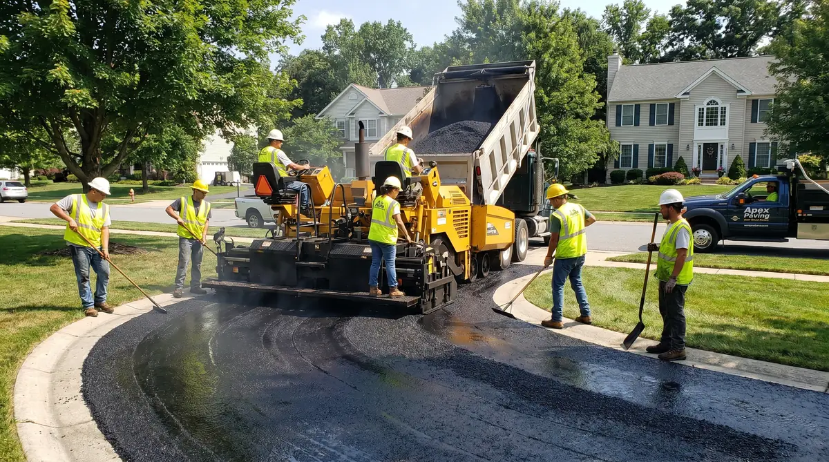 Professional asphalt paving contractor crew operating a paver machine on a residential driveway