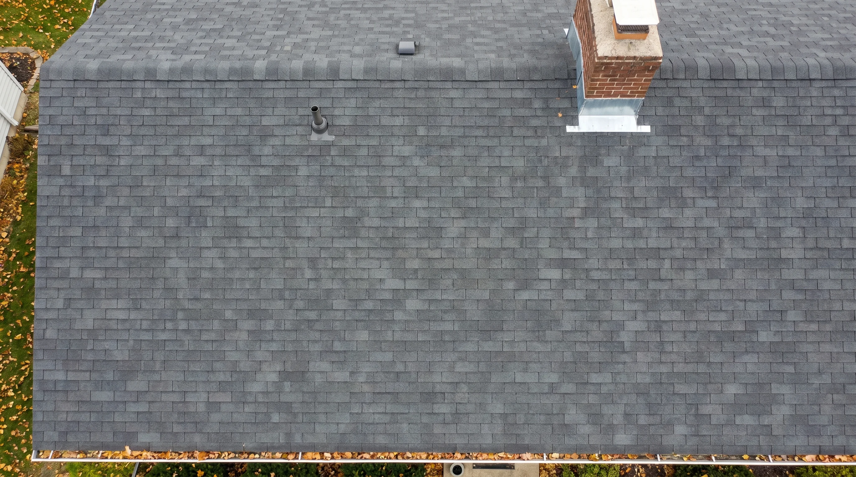 Aerial close-up of a well-maintained dark gray architectural asphalt shingle roof on a residential home in bright daylight showing clean uniform shingles