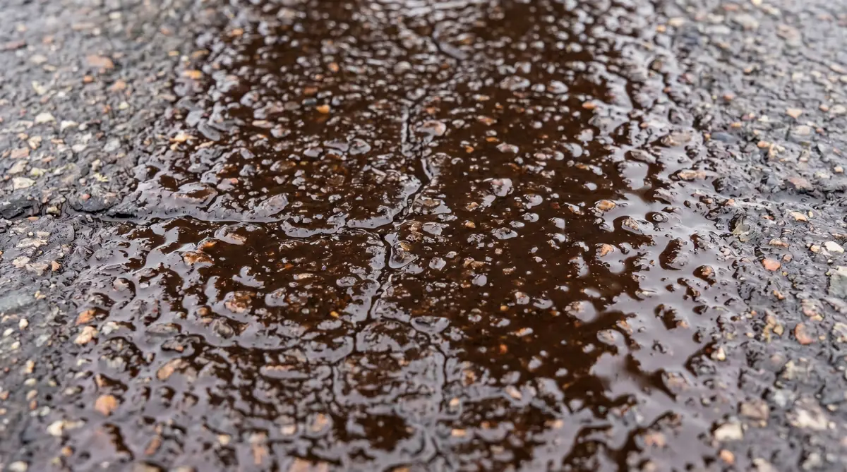 Close-up of fresh tack coat emulsion on asphalt surface showing brown liquid coating