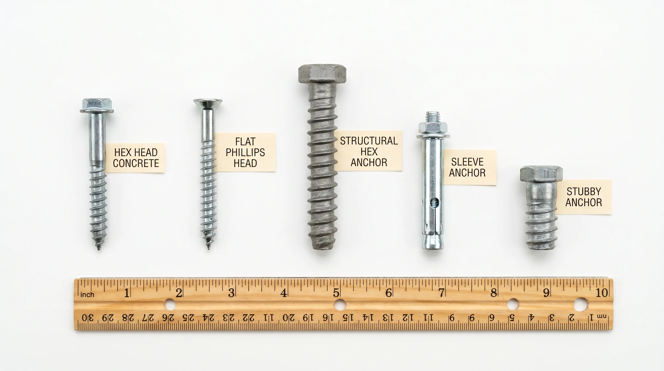 Flat lay of five different concrete screw types on white background — hex head, flat Phillips, large-diameter structural, sleeve-style, and short anchor screw with paper labels and ruler for scale