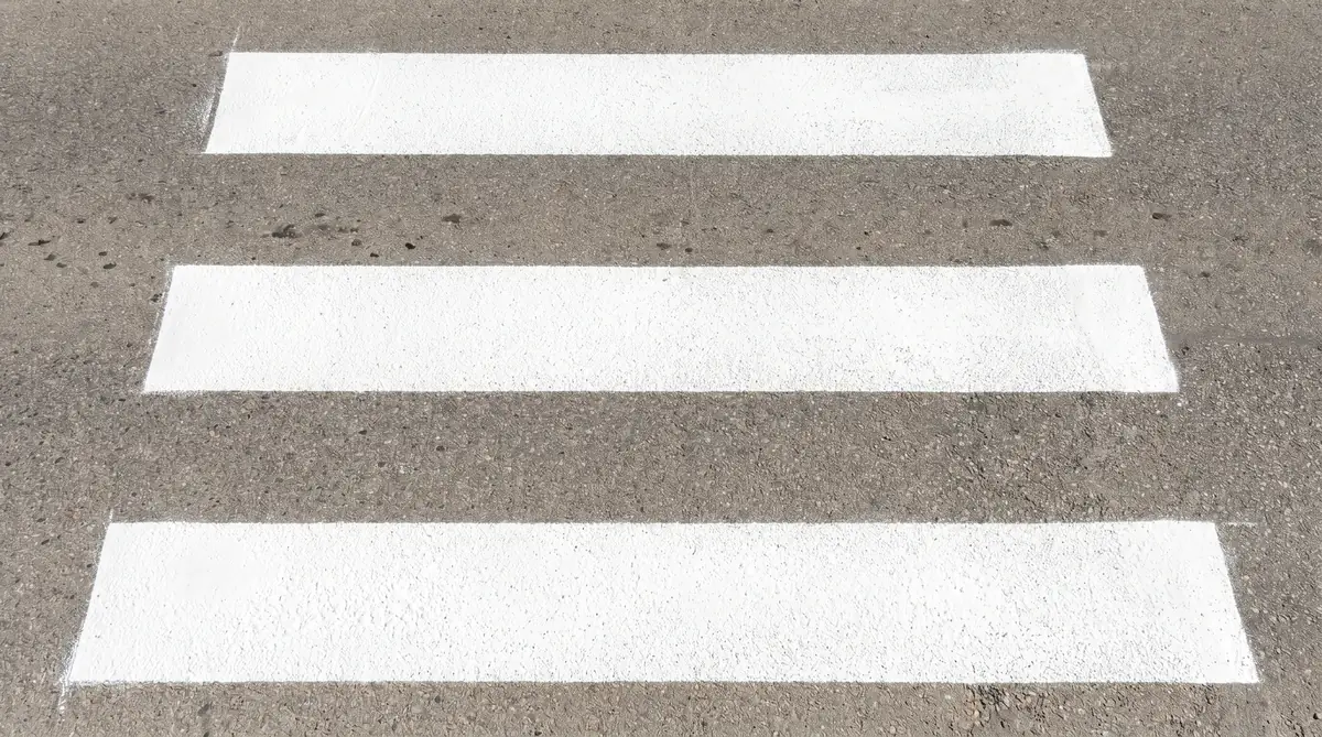 Overhead view of freshly applied thermoplastic crosswalk markings showing bold white parallel stripes with raised texture on asphalt